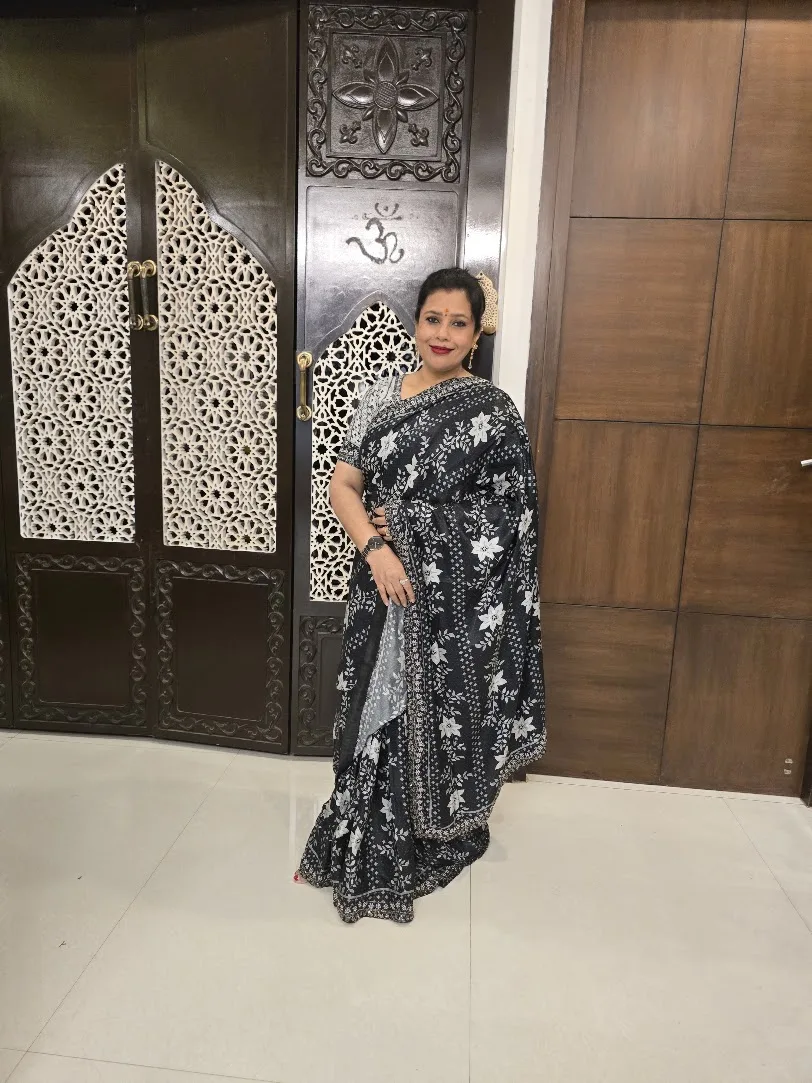 Seema in a black floral saree in front of carved wooden doors