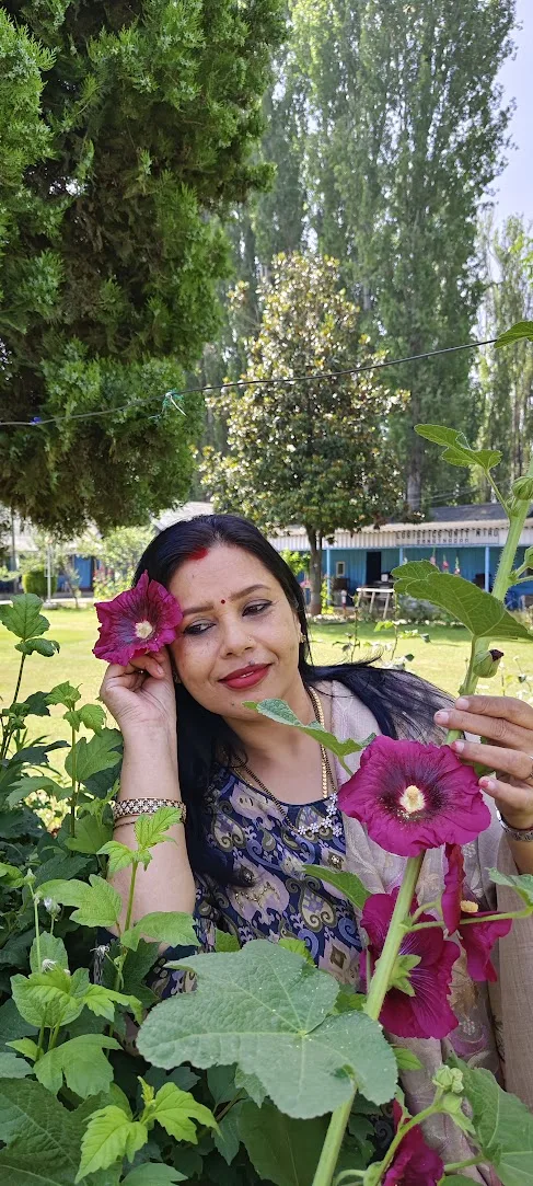 Seema in a garden holding a pink hollyhock flower