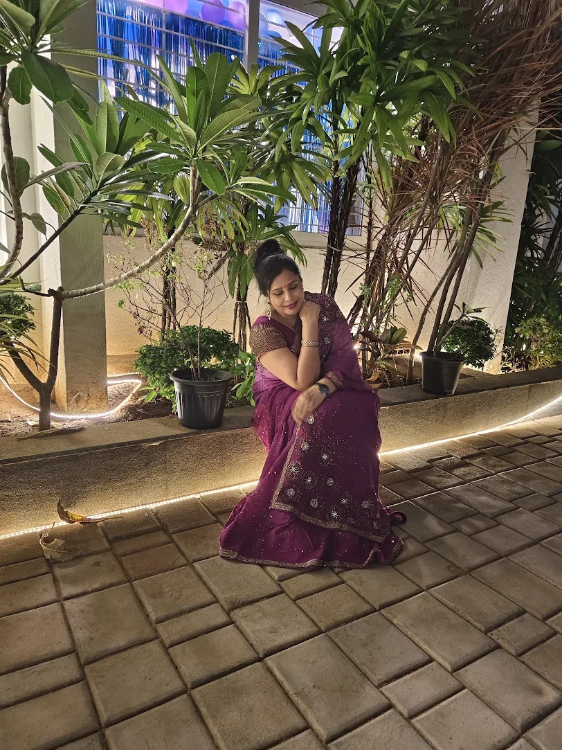 Seema seated in a purple saree beside garden lights at night